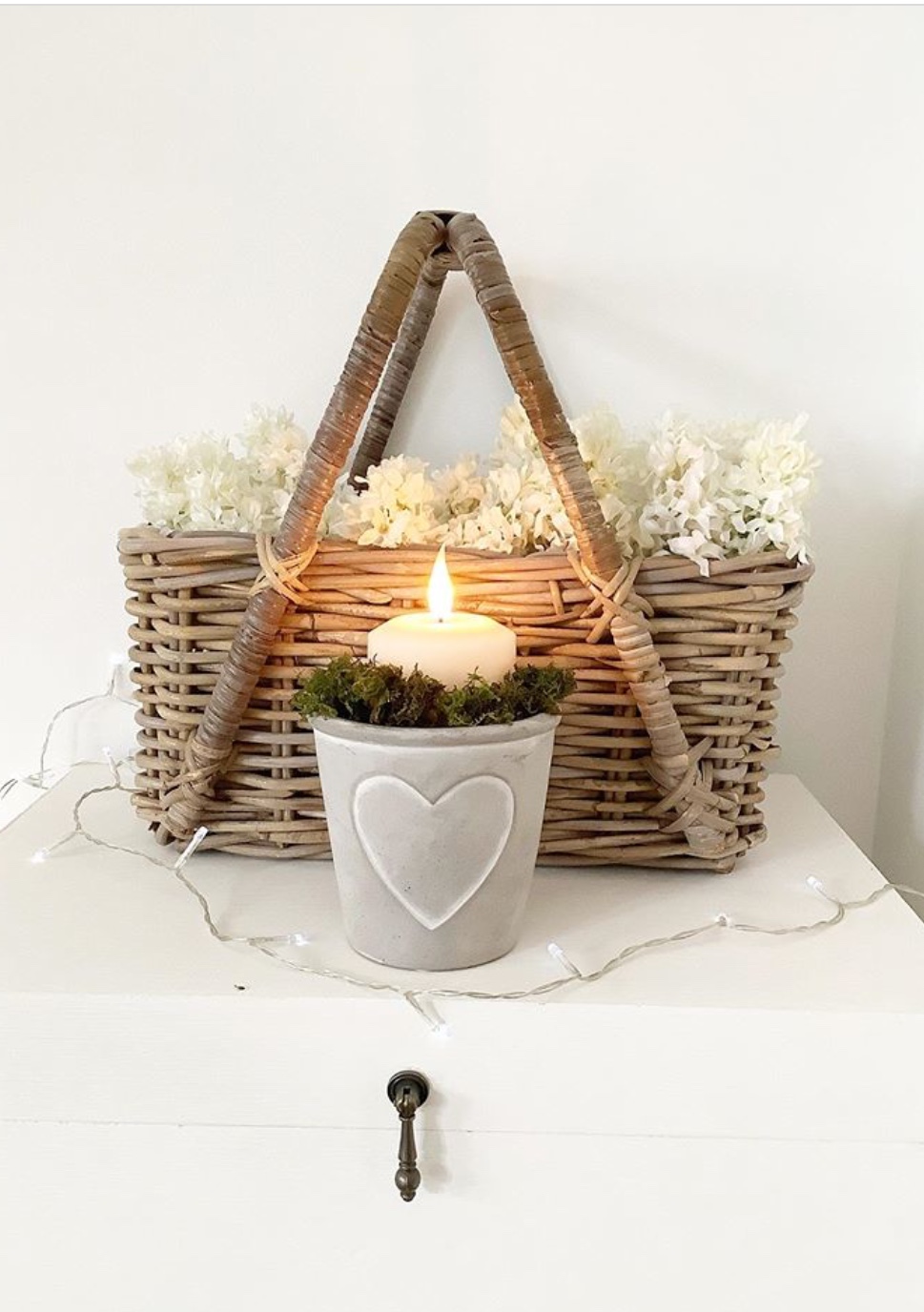 Luxury LED pillar candle inside a plantpot surrounded by moss with a basket of foliage in the background