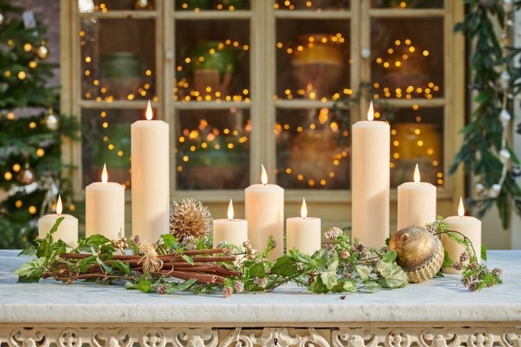 A cluster of luxury LED pillar candles of varying heights on a table surrounded by foliage
