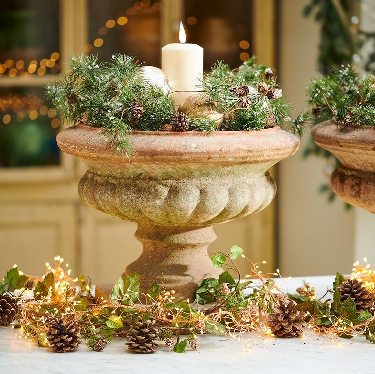 A luxury LED pillar candle in an antique urn surreounded by Christmas foliage and twinkly lights